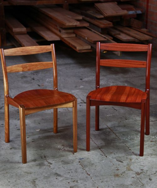 A pair of Australian designed and made low back dining chairs, one in blackwood and one in jarrah in a woodworking workshop.
