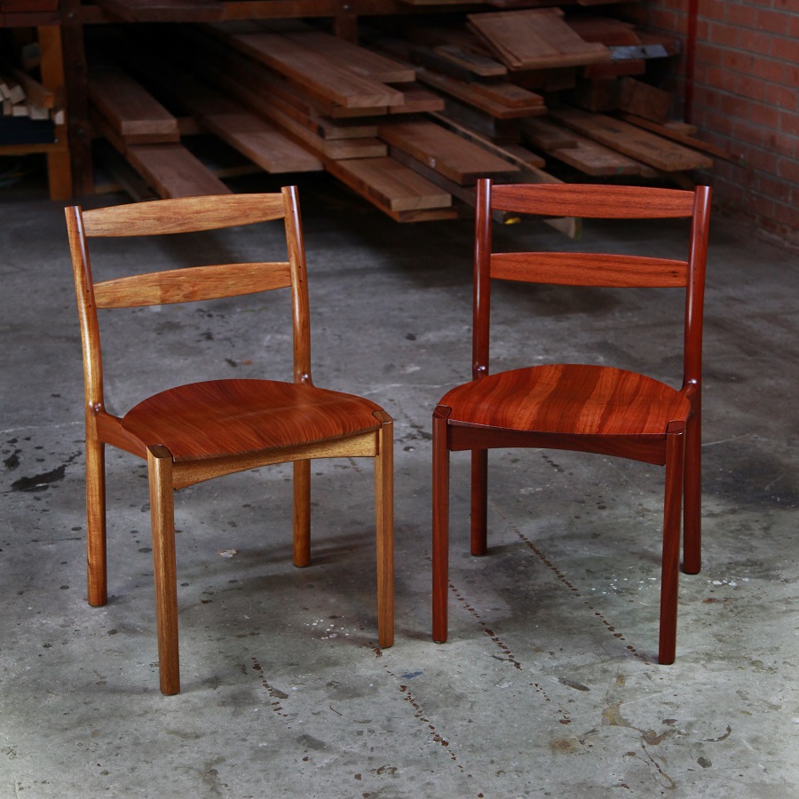 A pair of Australian designed and made low back dining chairs, one in blackwood and one in jarrah in a woodworking workshop.