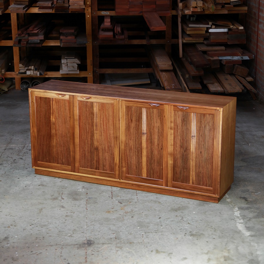 A photograph of a four door cabinet in a woodworking workshop with natural light highlighting the warm grain.