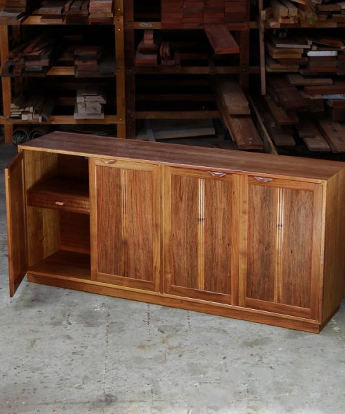 A photograph of a four door cabinet in a woodworking workshop with natural light highlighting the warm grain.