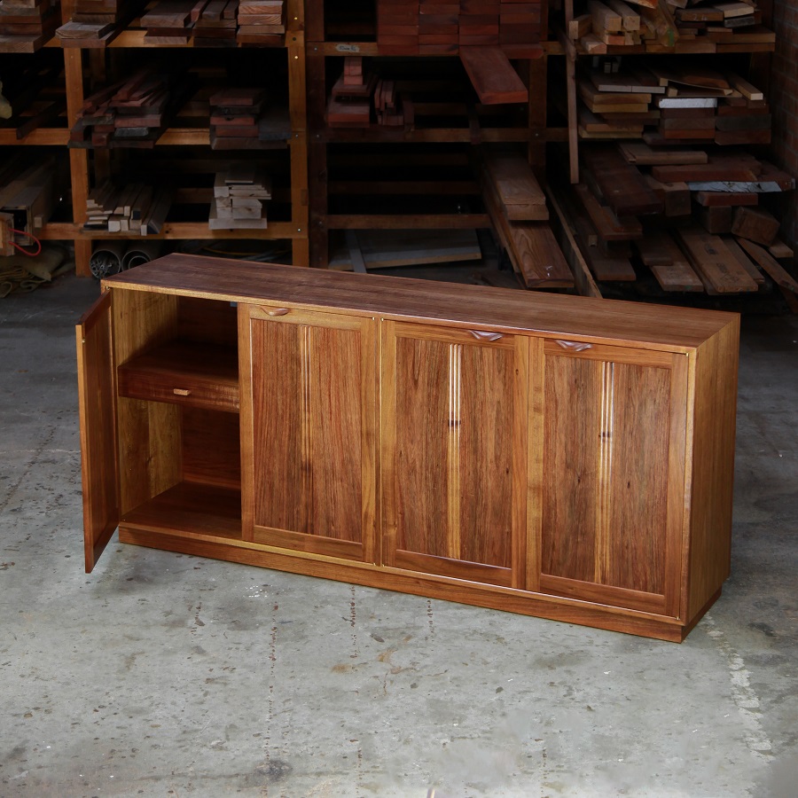 A photograph of a four door cabinet in a woodworking workshop with natural light highlighting the warm grain.