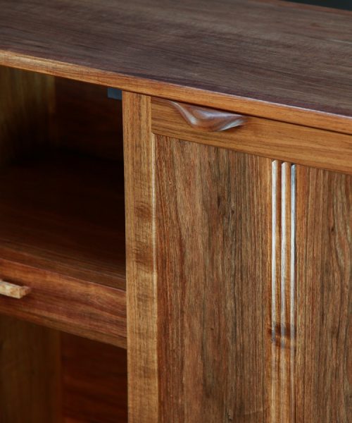 A photograph of a four door cabinet in a woodworking workshop with natural light highlighting the warm grain.