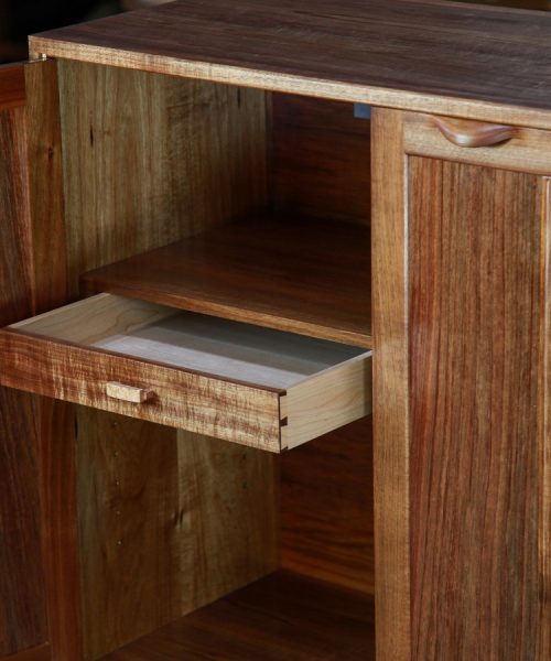 A photograph of a four door cabinet in a woodworking workshop with natural light highlighting the warm grain.