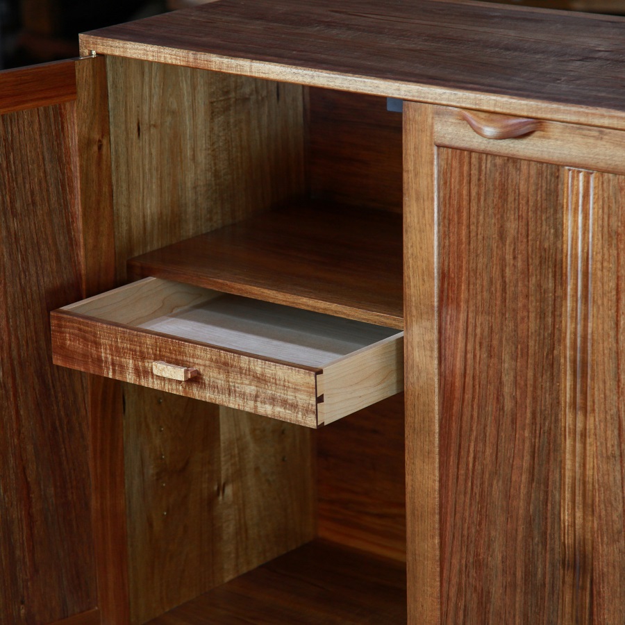 A photograph of a four door cabinet in a woodworking workshop with natural light highlighting the warm grain.