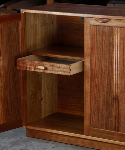 A photograph of a four door cabinet in a woodworking workshop with natural light highlighting the warm grain.