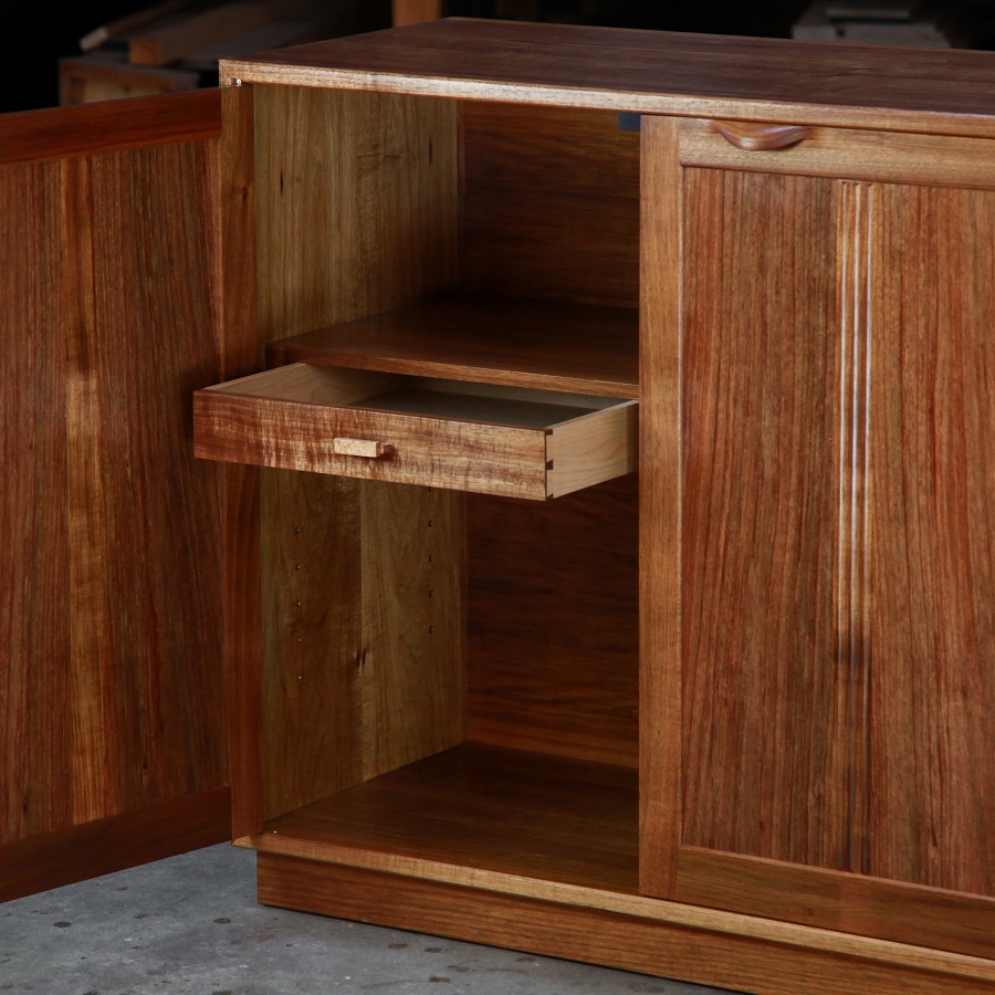 A photograph of a four door cabinet in a woodworking workshop with natural light highlighting the warm grain.