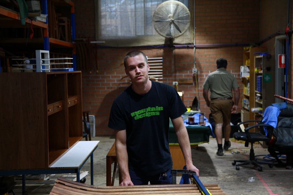a young woodworker in a workshop with stool components.