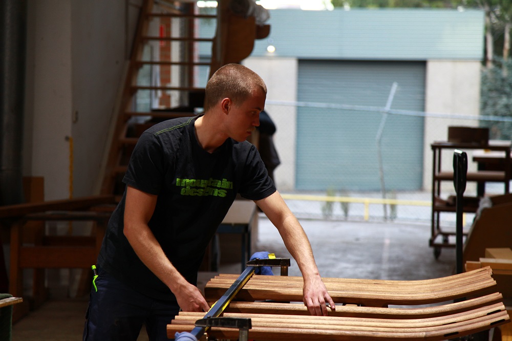 a young woodworker in a workshop with stool components.