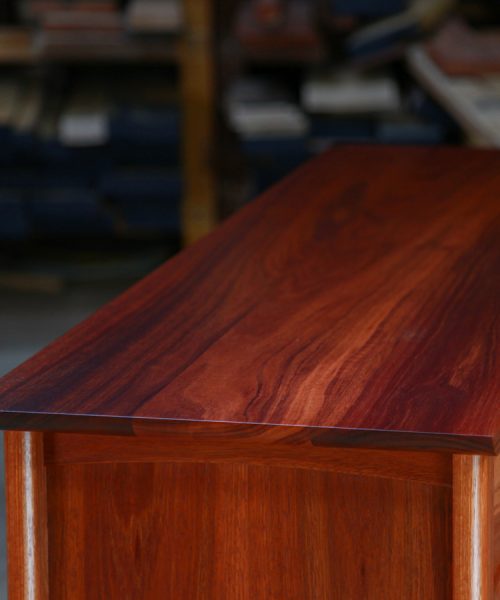 Top detail of a fine jarrah and rock maple Lakeview 3 chest of drawers in front of a timber rack in a workshop.
