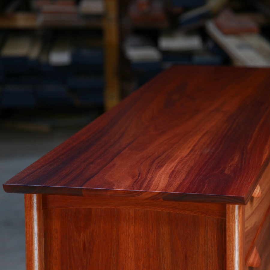 Top detail of a fine jarrah and rock maple Lakeview 3 chest of drawers in front of a timber rack in a workshop.
