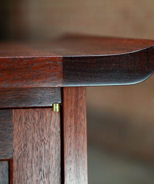 The light shines of the top detail of a jarrah cabinet featuring a Brusso knife hinge.