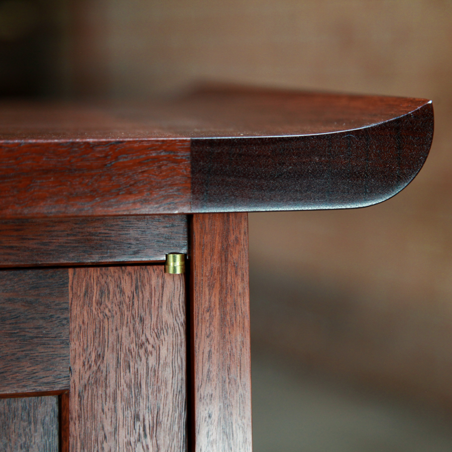 The light shines of the top detail of a jarrah cabinet featuring a Brusso knife hinge.
