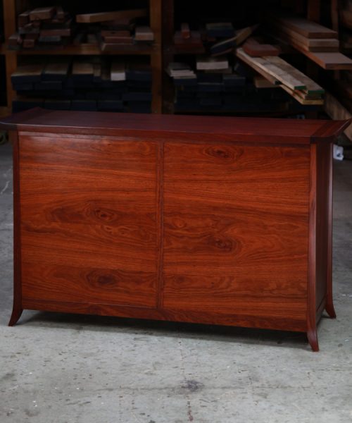 The rear of a beautiful jarrah cabinet sitting in a workshop in front of a timber rack.