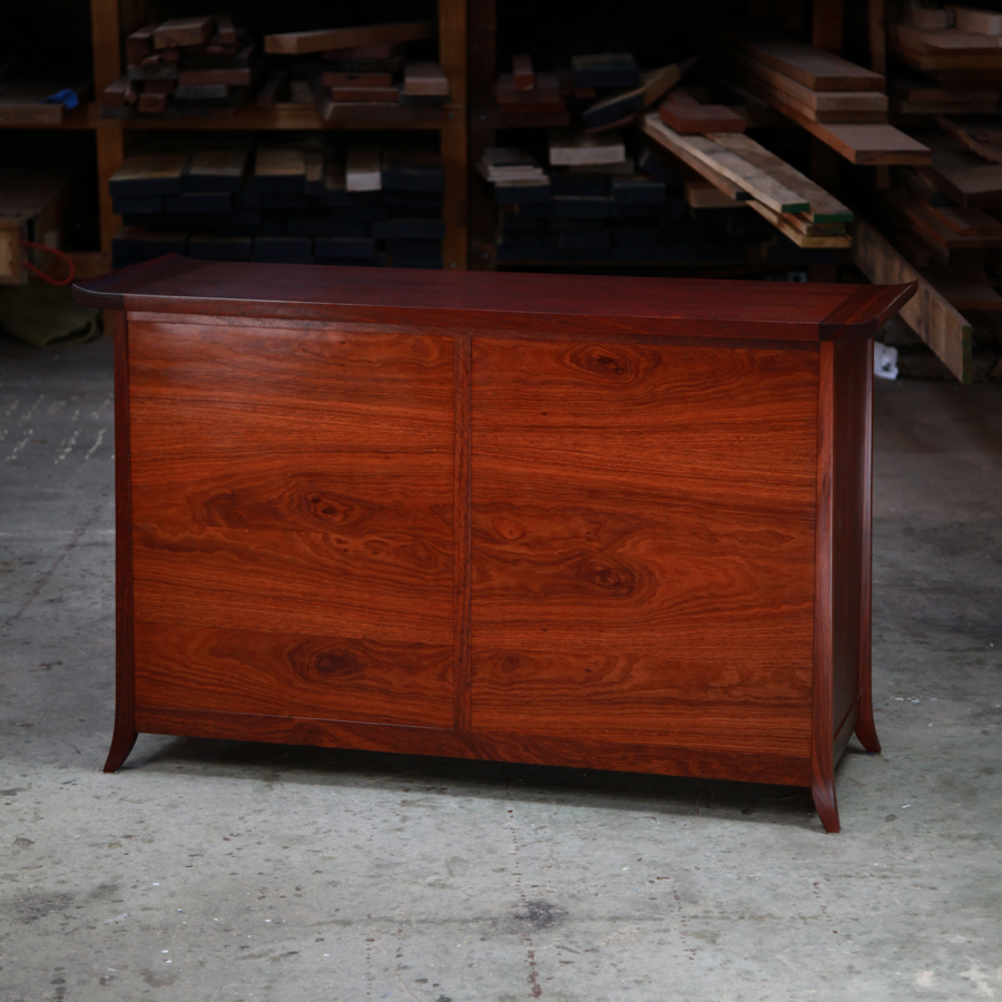 The rear of a beautiful jarrah cabinet sitting in a workshop in front of a timber rack.