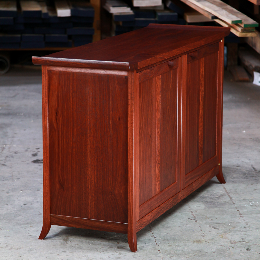 The side view of a beautiful jarrah cabinet sitting in a workshop in front of a timber rack.