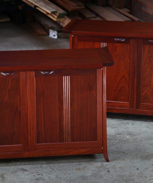 A matching pair of jarrah cabinets sit in a workshop in front of a timber rack.