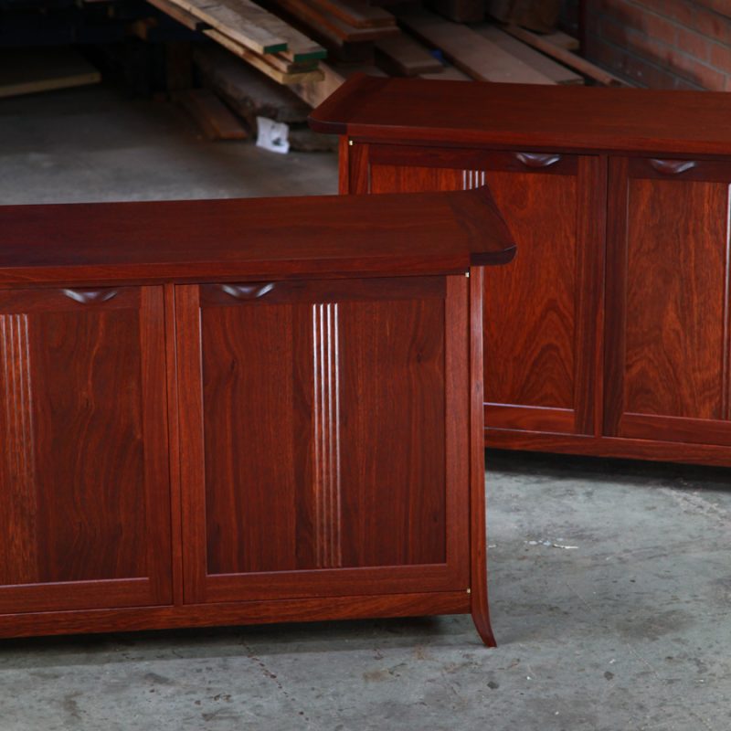 A matching pair of jarrah cabinets sit in a workshop in front of a timber rack.