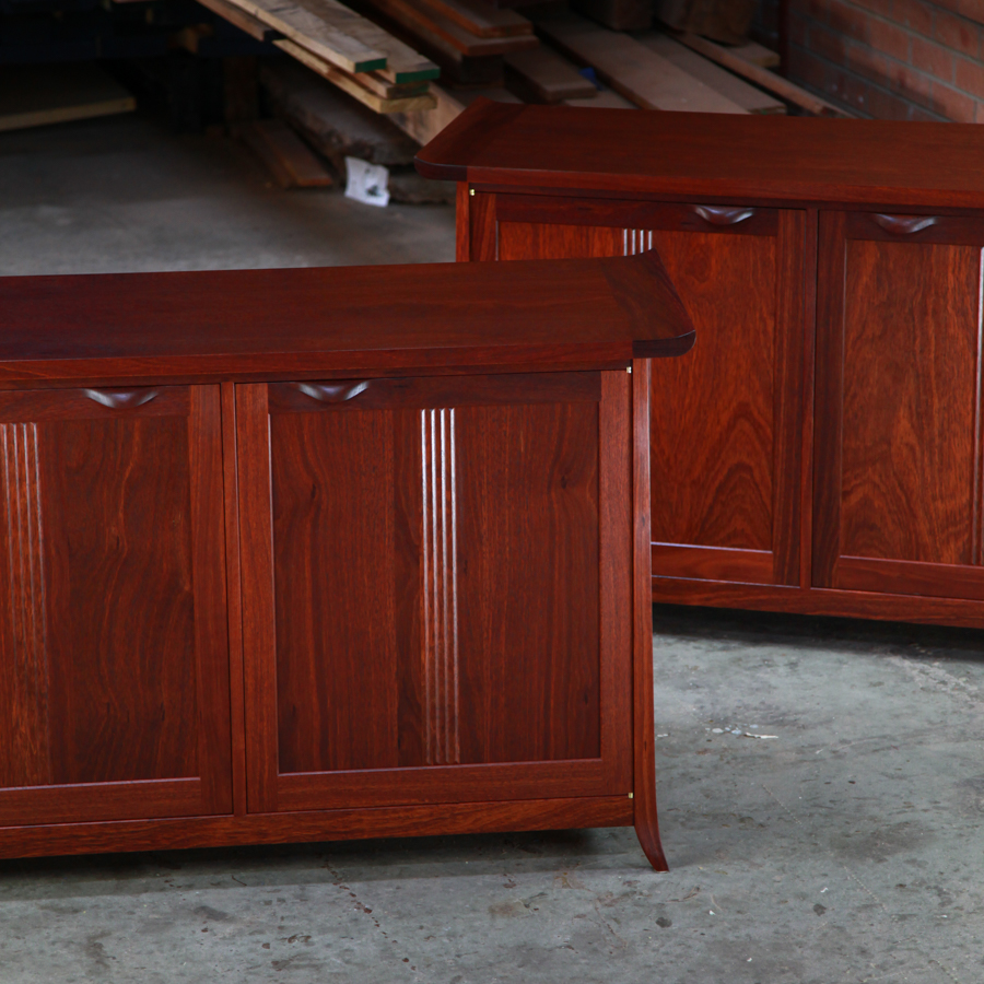 A matching pair of jarrah cabinets sit in a workshop in front of a timber rack.