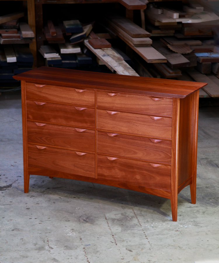 A beautiful jarrah cabinet sits in front of a timber rack in a workshop.