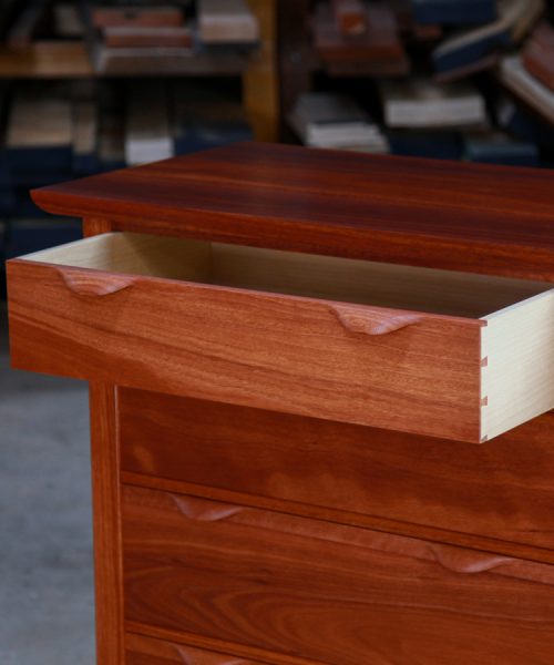 An open drawer in a fine jarrah and rock maple Lakeview 3 chest of drawers in front of a timber rack in a workshop.